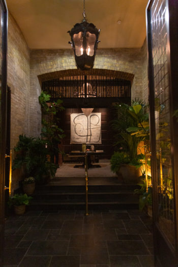 Entrance to NoMad London. Black lantern on the ceiling, pale yellow brick walls with steps to the hotel reception